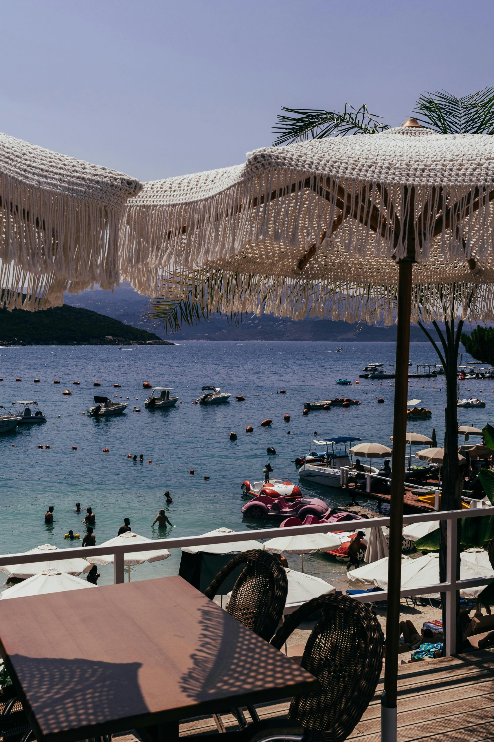 Relaxant paysage de plage avec des parasols, des bateaux et des baigneurs dans un cadre côtier serein.