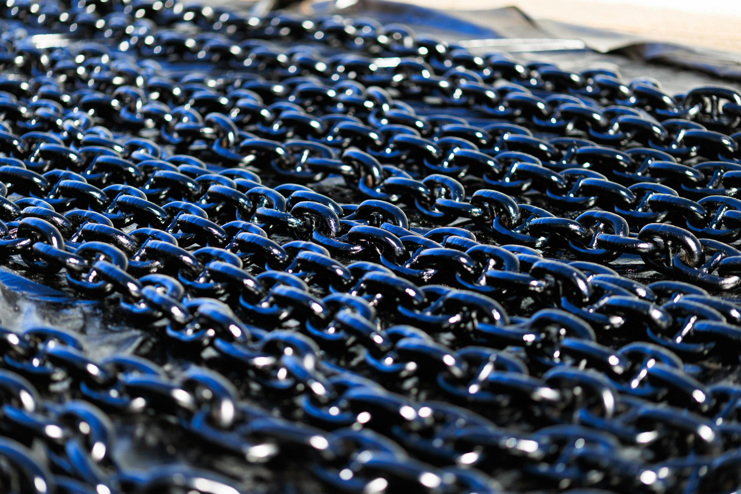 Détail d'une vue rapprochée de chaînes métalliques industrielles brillantes disposées en extérieur, mettant en valeur leur texture et leur qualité métallique.