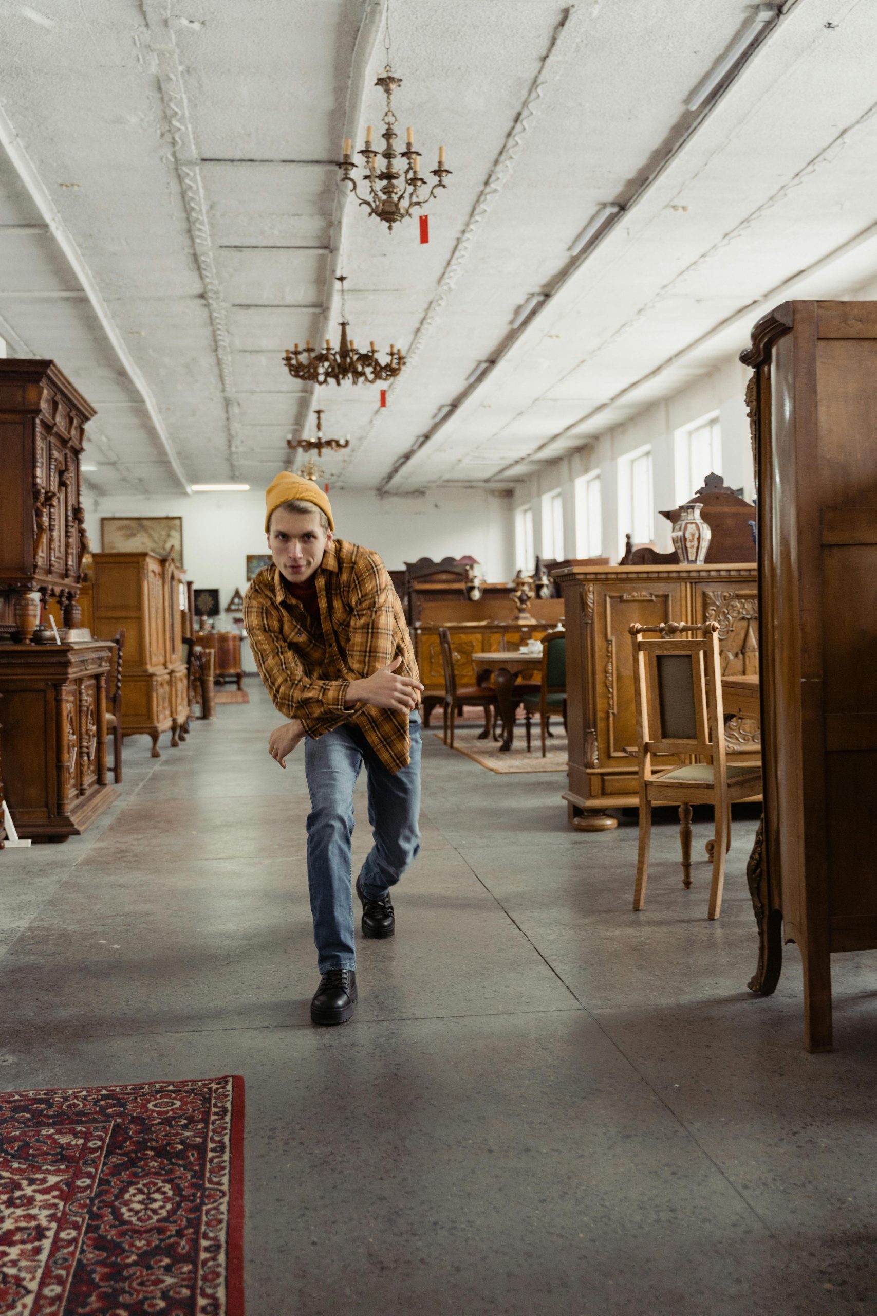 Un jeune homme pose de manière décontractée dans un magasin de meubles vintage, entouré de pièces en bois anciennes.