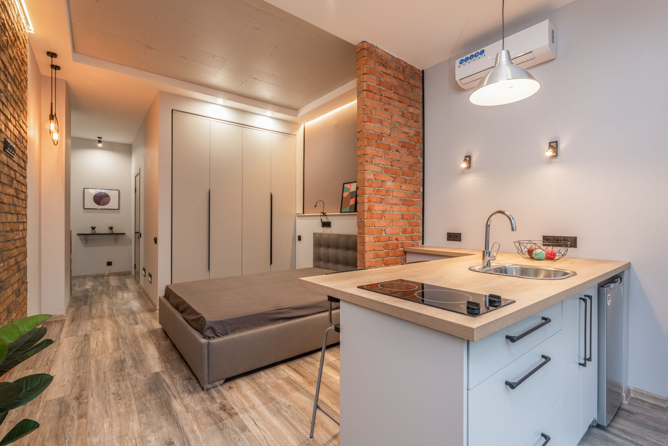 Miniature cuisine avec appareils modernes et chambre derrière une cloison en brique dans un petit appartement de style loft