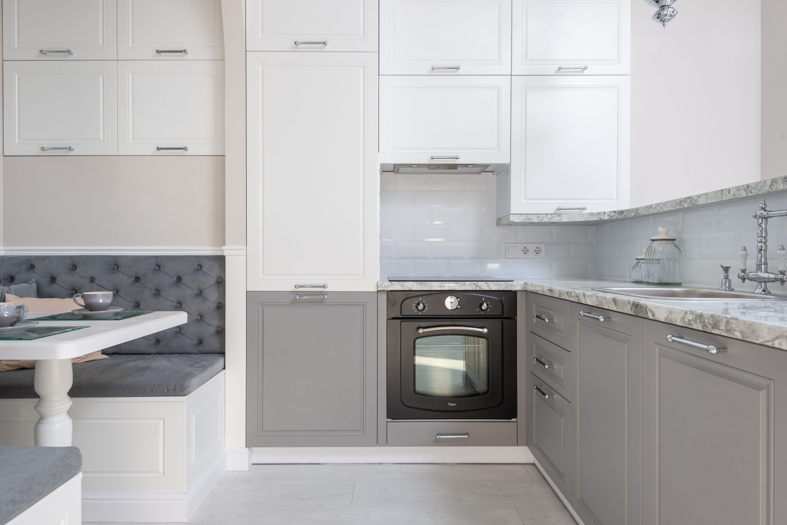 Served table with dishware placed near marble kitchen counter with white and gray cupboards and modern kitchenware in stylish apartment Table servie avec de la vaisselle placée près d'un comptoir de cuisine en marbre avec des placards blanc et gris et des appareils de cuisine modernes dans un appartement élégant