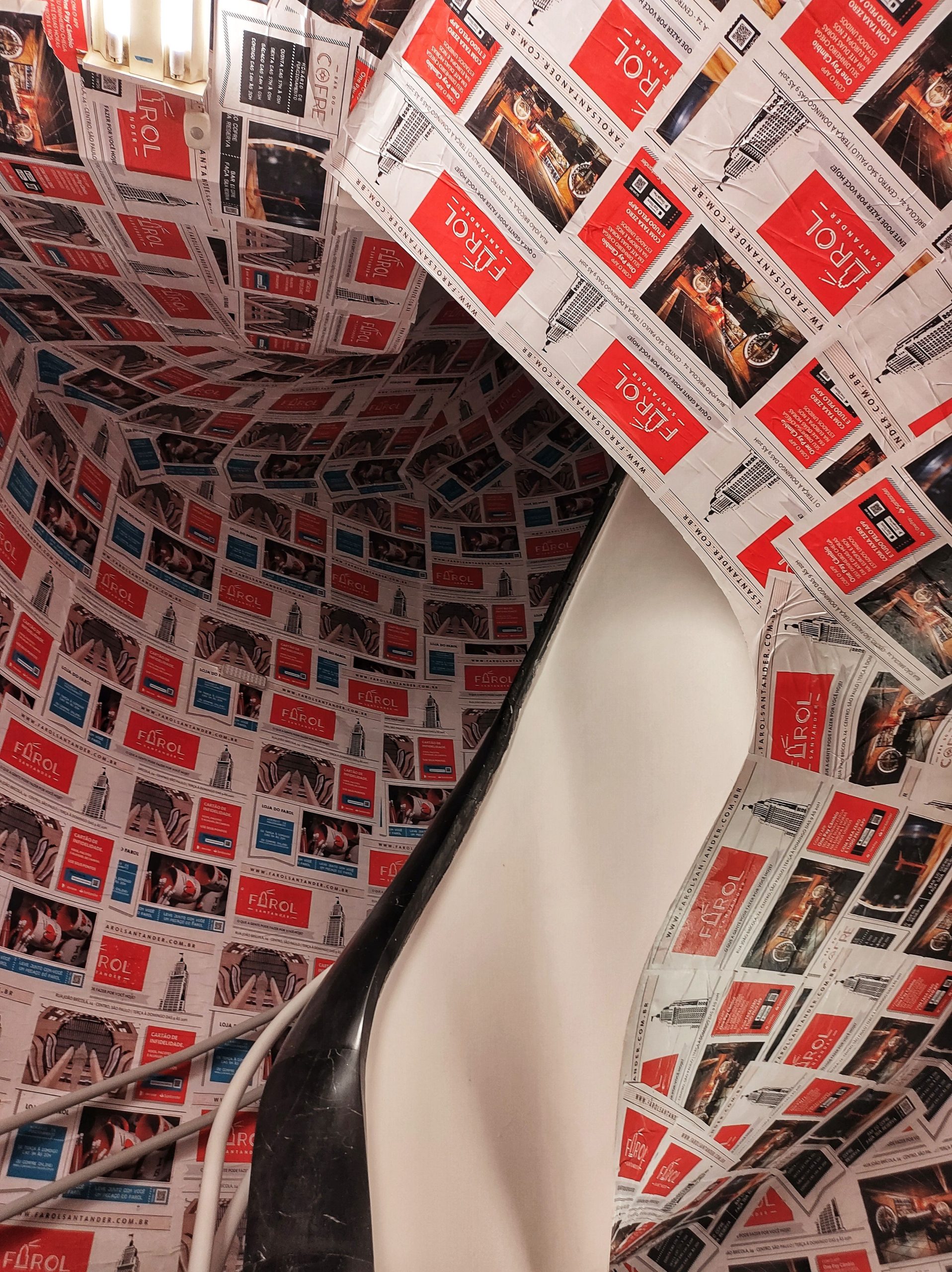 Creative interior design with newspaper advertisements covering walls in a spiral staircase. Design intérieur créatif avec des annonces publicitaires de journaux couvrant les murs d'un escalier en spirale.