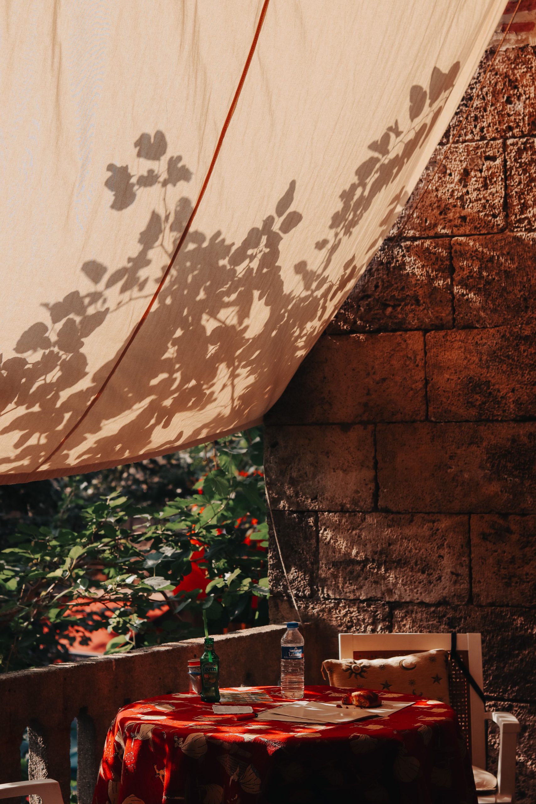 Relaxing outdoor patio with a sunlit fabric canopy casting leaf shadows, perfect for summer afternoons. Un patio extérieur relaxant avec un auvent en tissu ensoleillé projetant des ombres de feuilles, parfait pour les après-midi d'été.