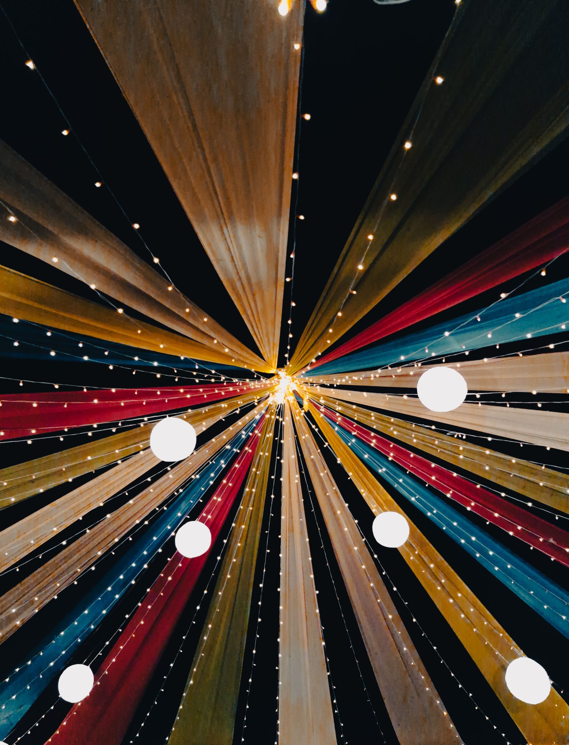 Vibrant drapes and fairy lights create a stunning ceiling design during a nighttime event. Des draperies vibrantes et des guirlandes féeriques créent un design de plafond époustouflant lors d'un événement nocturne.