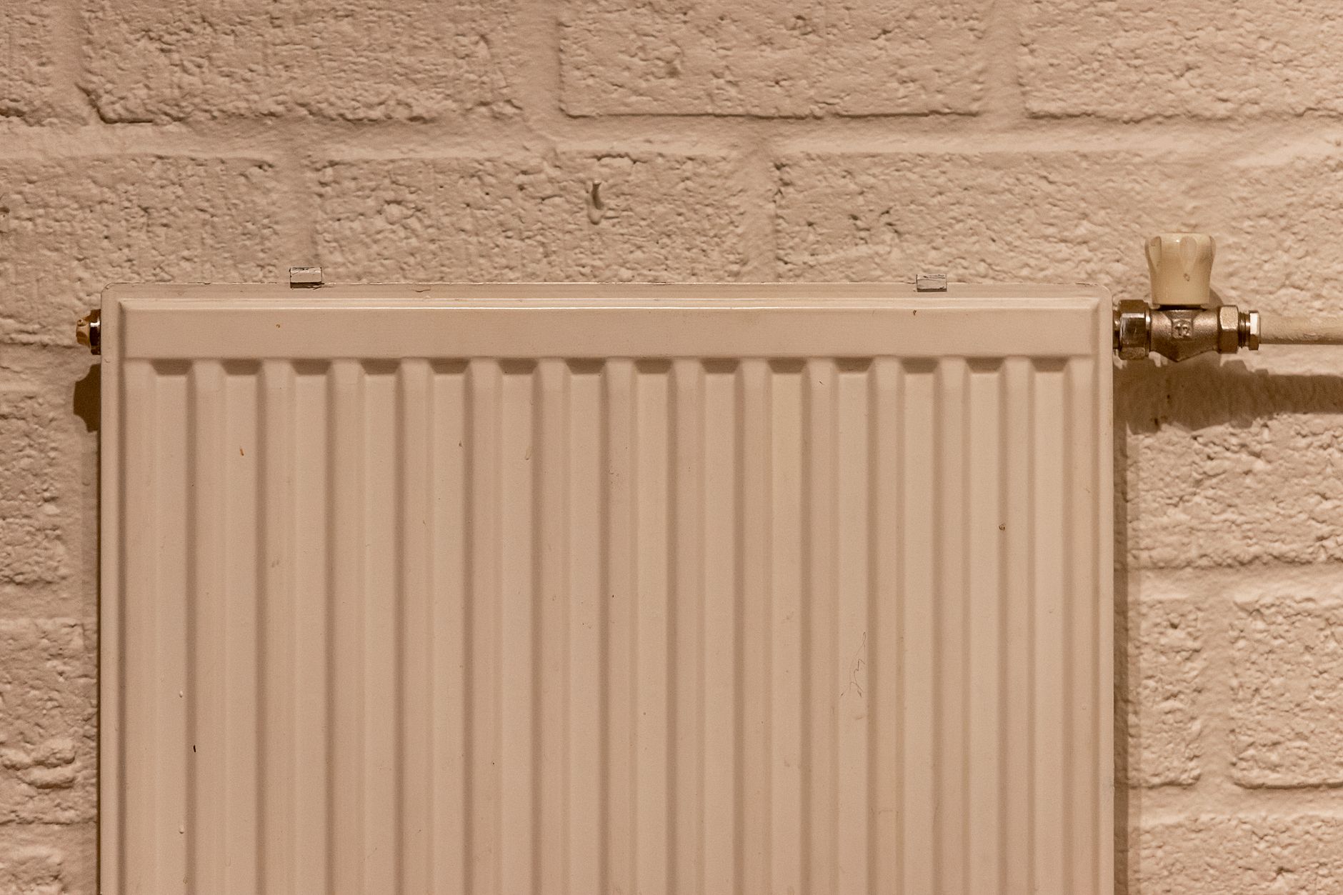 Radiateur blanc raccordé à un mur en briques